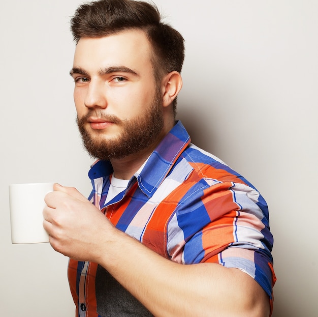 Jeune homme barbu avec une tasse de café sur fond gris