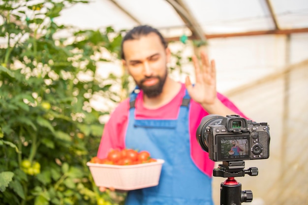 Jeune homme barbu tenant une tomate et serrant la main à la caméra