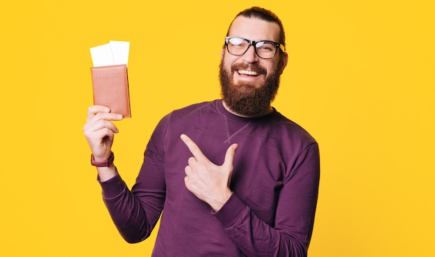 Un jeune homme barbu tient un passeport avec des billets et le montre en souriant