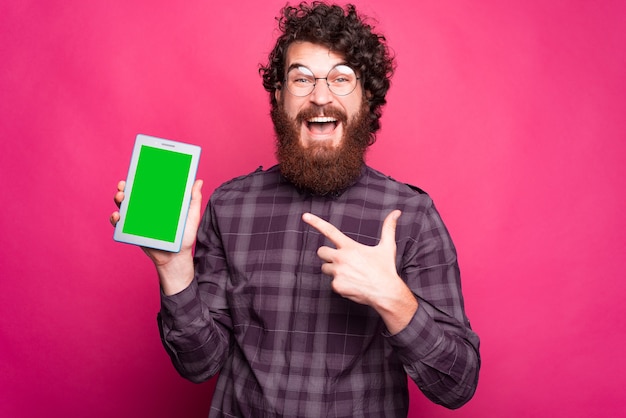 Jeune homme barbu tient une tablette et le pointe du doigt