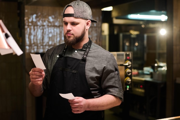 Jeune homme barbu en uniforme regardant à travers les points de recette sur papier