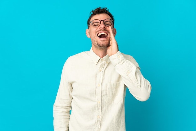 Jeune homme beau caucasien isolé sur bleu criant avec la bouche grande ouverte