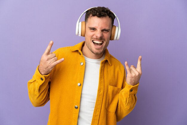 Jeune homme beau caucasien isolé écoute de la musique faisant un geste rock