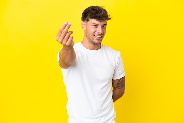 Jeune homme beau caucasien isolé sur fond jaune faisant un geste d'argent