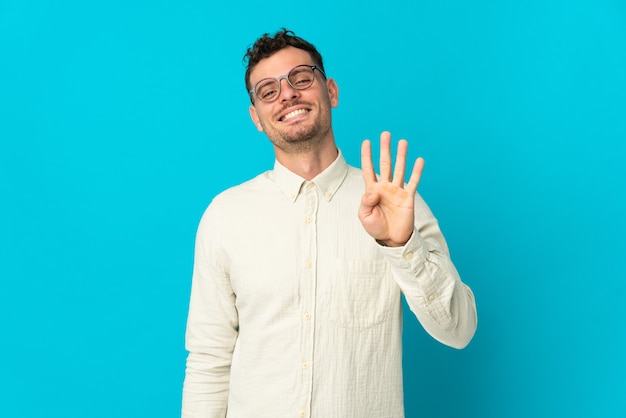 Jeune homme beau caucasien isolé sur un mur bleu heureux et comptant quatre avec les doigts