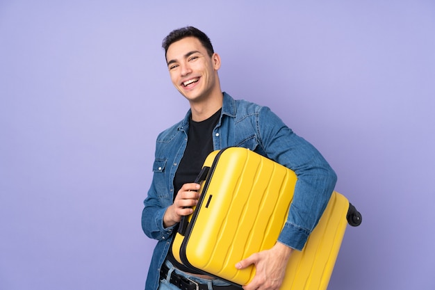 Jeune homme beau caucasien sur mur violet en vacances avec valise de voyage