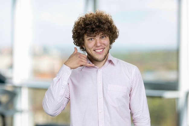 Photo jeune homme beau avec des cheveux bouclés montre appelez-moi geste