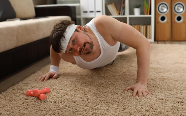 Un jeune homme beau avec un excès de poids fait le premier entraînement physique à la maison sur le tapis wrung et il ery lourdement chargé ne stimule pas à perdre du poids