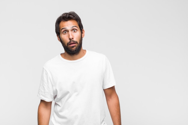 Jeune homme beau latin souriant joyeusement et avec désinvolture, regardant vers le bas et pointant vers la poitrine