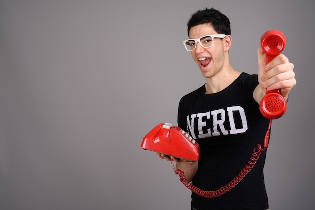 Jeune homme beau nerd avec des lunettes contre le gris