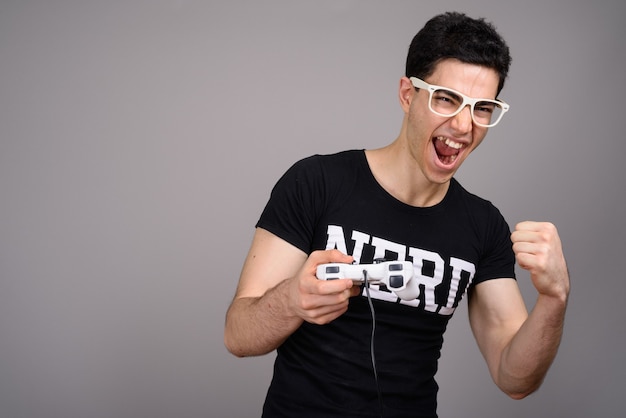 Jeune homme beau nerd avec des lunettes contre le gris