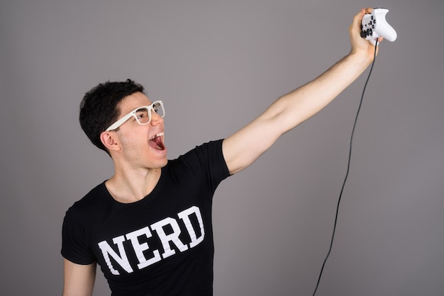 Jeune homme beau nerd avec des lunettes contre le gris