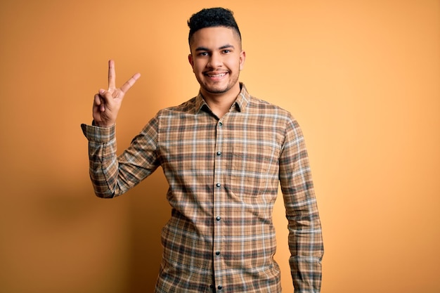 Jeune homme beau portant une chemise décontractée debout sur un fond jaune isolé montrant et pointant vers le haut avec les doigts numéro deux tout en souriant confiant et heureux