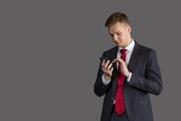 Jeune homme beau et séduisant en costume à l'aide de téléphone, communiquant sur smartphone, lecture de nouvelles, message. concept d'entreprise.