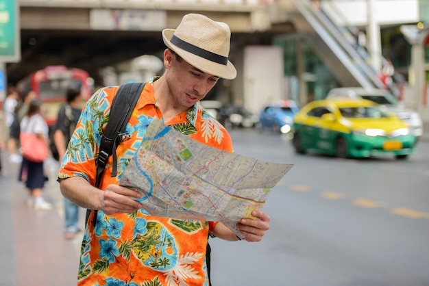 Jeune homme beau touriste avec sac à dos de lecture de la carte dans les rues de la ville