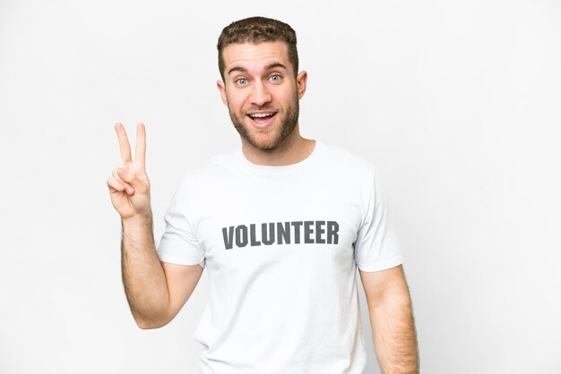 Jeune homme bénévole sur fond blanc isolé souriant et montrant le signe de la victoire