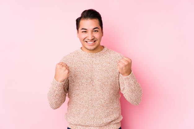 Jeune homme bien roulé posant dans un mur rose isolé acclamant insouciant et excité. Concept de victoire.