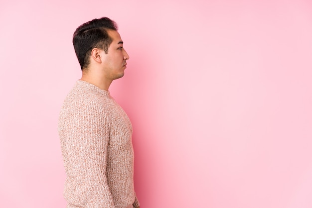 Jeune homme bien roulé posant dans un mur rose isolé regardant à gauche, pose de côté.