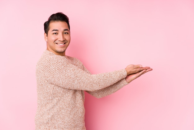 Jeune homme bien roulé posant dans un mur rose isolé tenant un espace copie sur une paume.