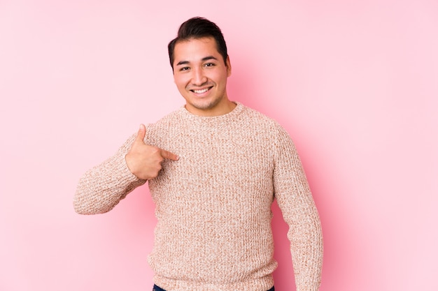 Jeune homme bien roulé posant dans un mur rose personne isolée pointant à la main vers un espace copie de chemise, fier et confiant