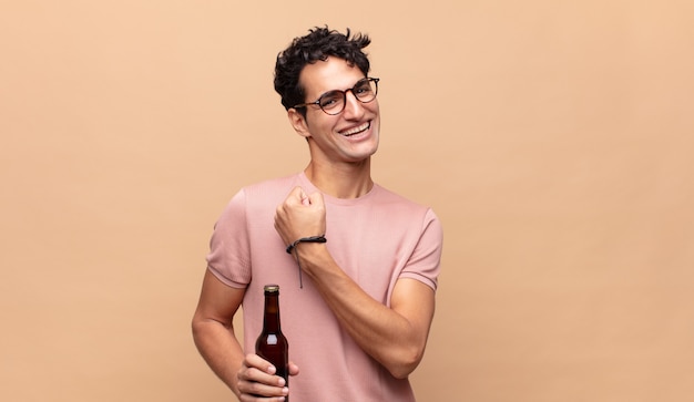 Jeune homme avec une bière se sentant heureux, positif et réussi, motivé face à un défi ou célébrant de bons résultats
