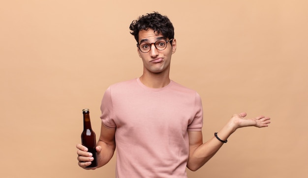 Jeune homme avec une bière se sentant perplexe et confus, doutant, pesant ou choisissant différentes options avec une expression drôle