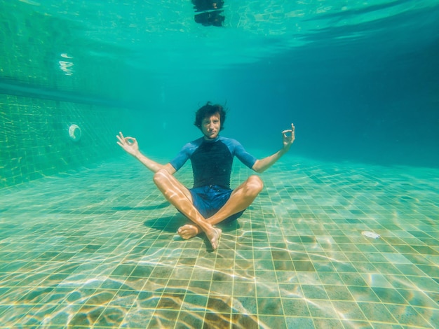 Jeune homme en bikini noir en position de yoga sous l'eau dans un aquarium de plongée, photo de tout le corps, vue de face.