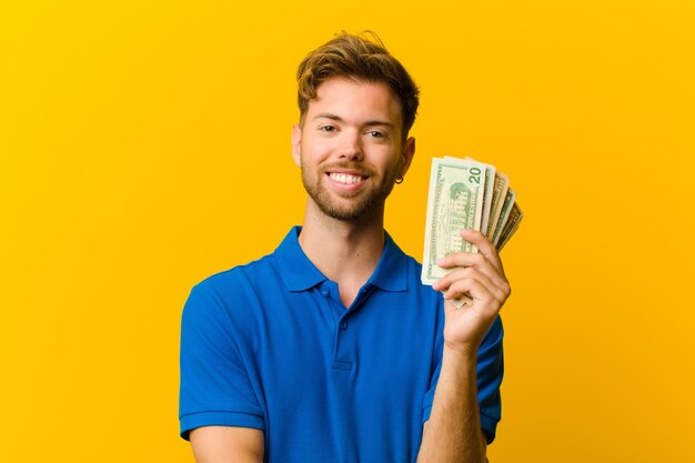 Jeune homme avec des billets contre le mur orange