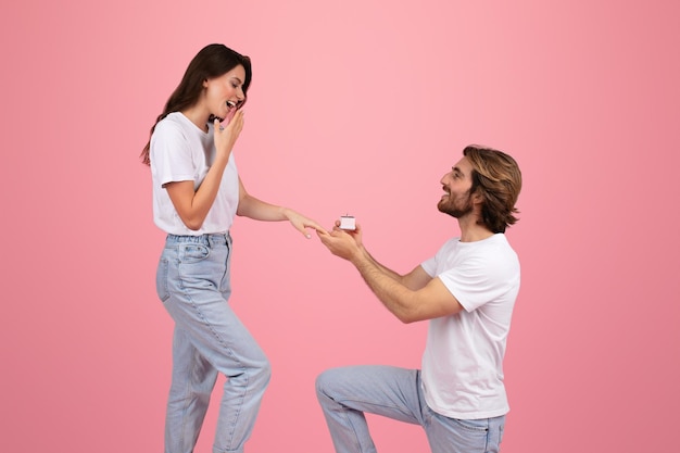Un jeune homme blanc heureux sur ses genoux donne la boîte à bagues à une femme surprise.