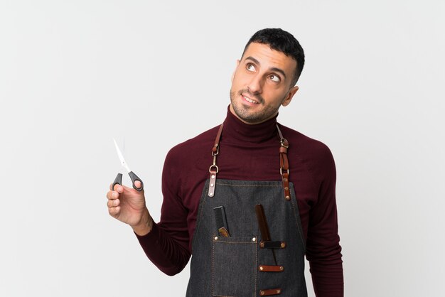 Jeune homme sur blanc isolé avec une robe de coiffeur ou coiffeur levant