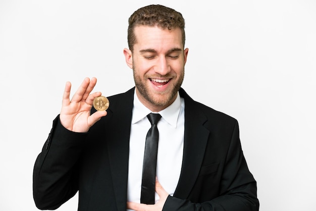 Jeune homme blond d'affaires tenant un bitcoin sur fond blanc isolé souriant beaucoup