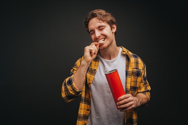 Jeune homme blond en chemise jaune mange des chips