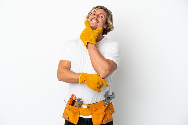 Jeune homme blond électricien isolé sur un mur blanc heureux et souriant