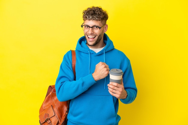 Jeune homme blond étudiant isolé sur fond jaune célébrant une victoire