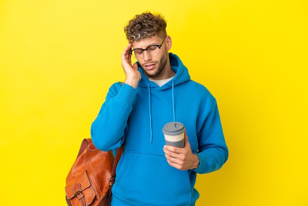 Jeune homme blond étudiant isolé sur fond jaune avec mal de tête