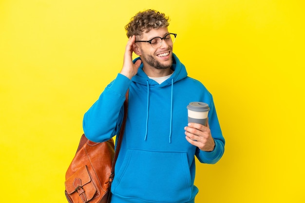 Jeune homme blond étudiant isolé sur fond jaune souriant beaucoup