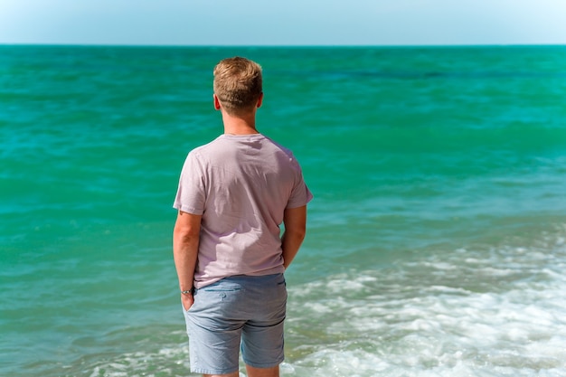 Un jeune homme blond marche sur la plage près de l'océan ou de la mer azur Le concept d'un été heureux
