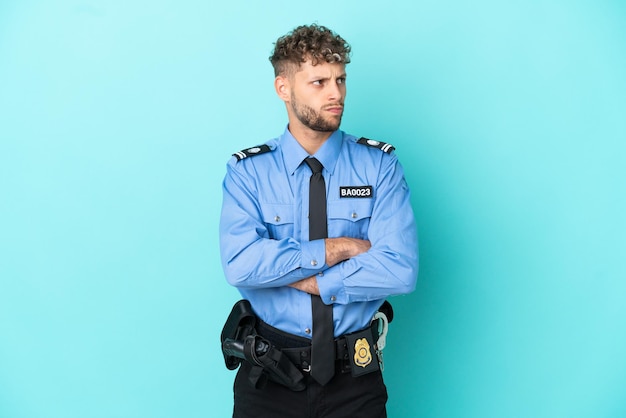 Jeune homme blond policier isolé blanc sur fond bleu faisant un geste de doute tout en soulevant les épaules