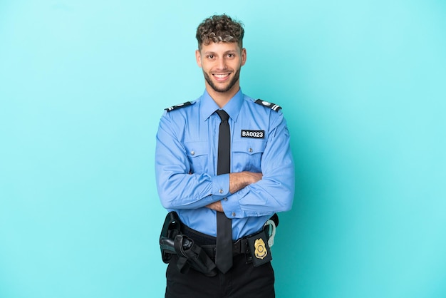 Jeune homme blond policier isolé blanc sur fond bleu en gardant les bras croisés en position frontale