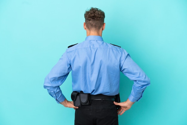 Jeune homme blond policier isolé blanc sur fond bleu en position arrière