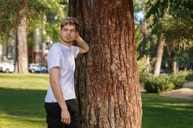 Un jeune homme blond s'appuyant sur l'arbre et regardant de côté