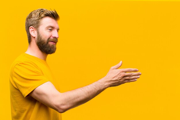 Jeune homme blond souriant, vous saluant et offrant une poignée de main