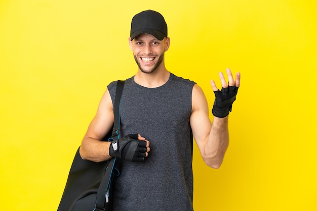 Jeune homme blond sport avec sac de sport isolé sur fond jaune faisant un geste de guitare