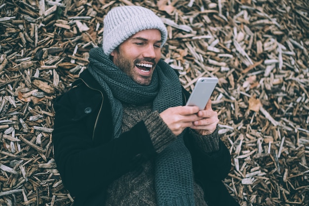 Jeune homme blond sur le téléphone portable se trouvant sur des morceaux de bois près du palais royal de Madrid en hiver