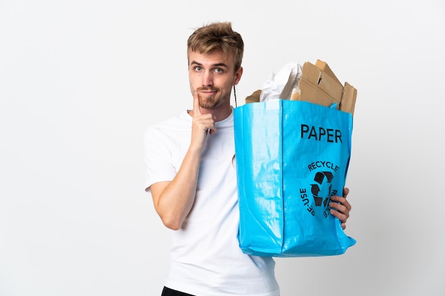 Jeune homme blond tenant un sac de recyclage plein de papier à recycler isolé sur fond blanc et pensée