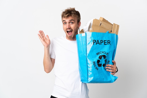 Jeune homme blond tenant un sac de recyclage plein de papier à recycler isolé