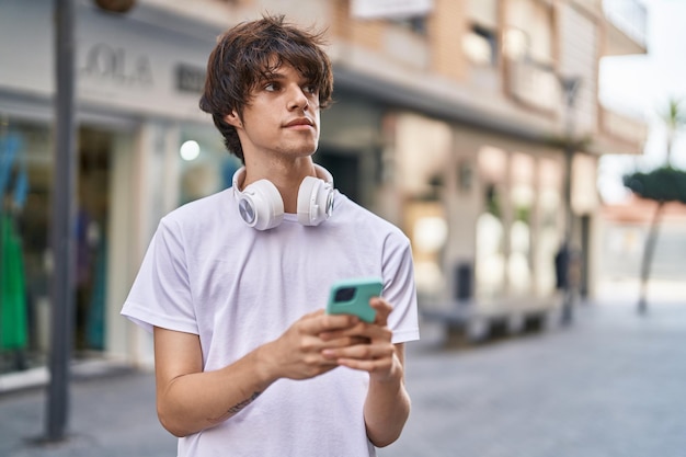 Jeune homme blond utilisant un smartphone avec une expression sérieuse dans la rue