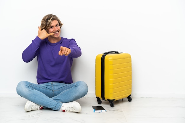 Jeune homme blond avec valise assis sur le sol faisant le téléphone