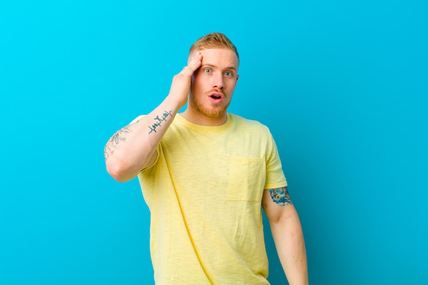 Jeune homme blond vêtu d'un t-shirt jaune, heureux, étonné et surpris, souriant et réalisant de bonnes et incroyables bonnes nouvelles