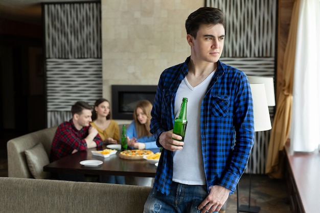 Jeune homme boit de la bière à partir d'une bouteille et regarde par la fenêtre dans un café